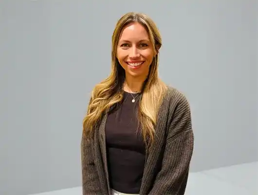 Head-and-shoulders portrait of a smiling blonde woman with wavy hair against a black background in a black top or blazer.