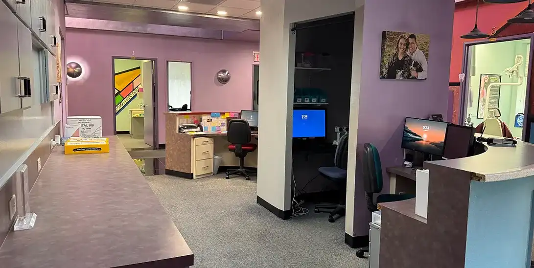 Reception area in a colorful office with purple walls, desks, and computer stations visible near a doorway to back rooms.